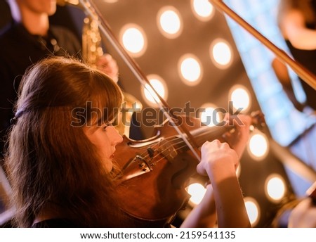 Beautiful young violinist on the background of a string orchestra in a loft interior. Close-up.