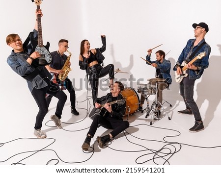 A young rock band of six people emotionally playing and singing on a white background