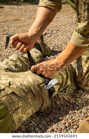 Army medics practice applying a tourniquet to the leg of a wounded soldier. Combat tactical equipment. Combat use Turnstile. The concept of military medicine. Royalty-Free Stock Photo #2159543691