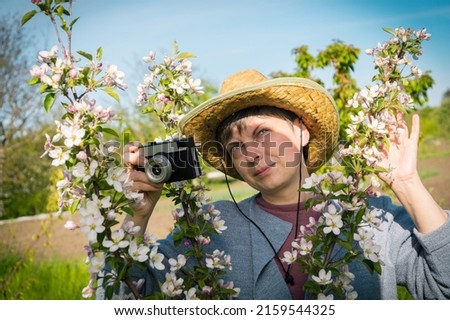 Photo hobby as a useful outdoor recreation. Pretty middle-aged woman in a hat holding a vintage camera among a blooming garden.