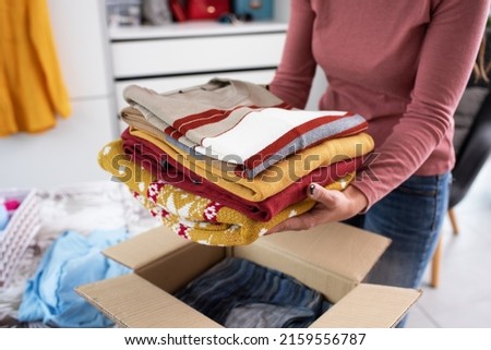 Young woman folding her clothes and packing them in a delivery box, she is changing her wardrobe Royalty-Free Stock Photo #2159556787