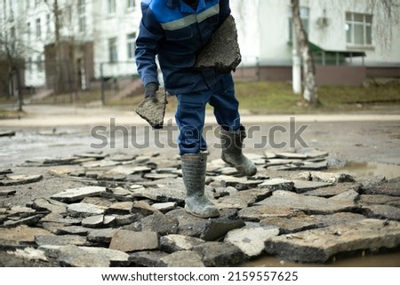 Worker throws rocks at road. Bad road repairs. Builder chooses construction debris. Man in blue special clothes.