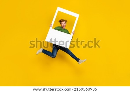Full length photo of funny excited guy dressed sweater holding white photo frame isolated yellow color background