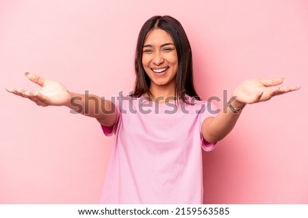 Young hispanic woman isolated on pink background feels confident giving a hug to the camera.