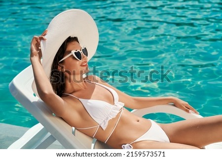 Side view of girl in white hat, sunglasses and bikini sunbathing on sunbed. Pretty slim female relaxing, having vacation, enjoying, Concept of summertime, leaisure and activity.