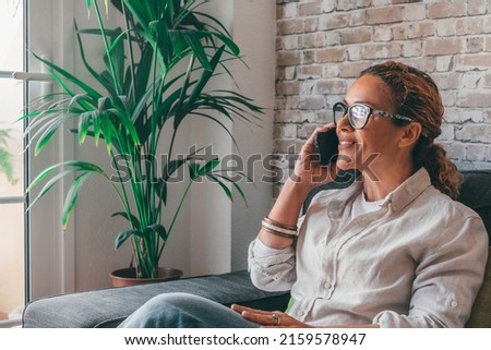 Smiling curly woman talking on the phone at home, happy young girl holds cellphone making answering call, attractive middle age having pleasant conversation chatting by mobile with friend