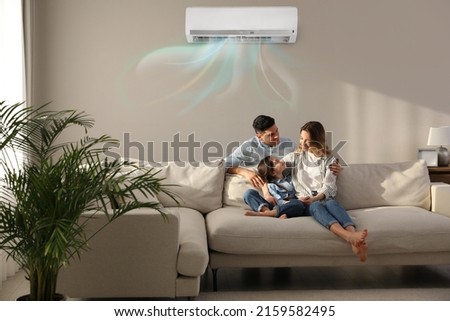 Happy family resting under air conditioner on beige wall at home Royalty-Free Stock Photo #2159582495