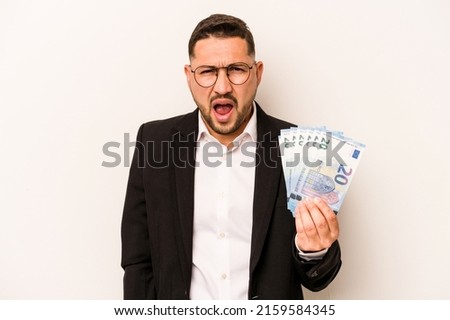 Business hispanic man holding banknotes isolated on white background screaming very angry and aggressive.