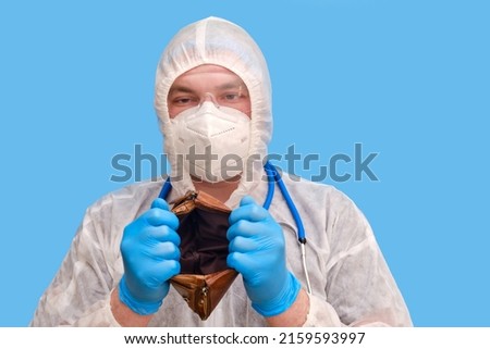 Man doctor medic in a protective suit uniform with goggles and face mask on a studio blue background. Paramedic in white antiviral protective clothing wearing an N95 respirator and safety glasses