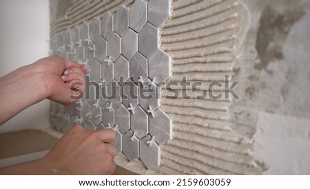 The master sets the crosses between the tiles. A worker installs a tile leveling system. Crosses for ceramic tiles. The tile is installing plastic crosses in the seams of ceramic tiles. Royalty-Free Stock Photo #2159603059