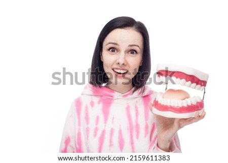smiling woman in a pink hoodie holds a dental jaw in her hand, white background. High quality photo