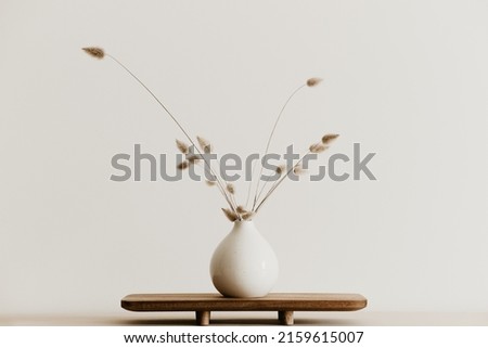 A bunch of  dried bunnytail flower in a white ceramic vase on a brown wooden board. Simple and minimal home decoration. White wall, copy space.  Royalty-Free Stock Photo #2159615007