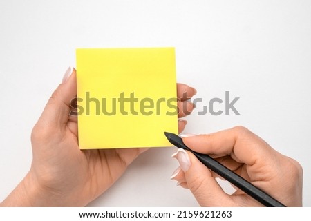 Mockup sticky Note Paper. Hand written notes black pencil on yellow sticker. white table background. woman hand writing on yellow sticky notes. female hand holding note paper and making note Royalty-Free Stock Photo #2159621263