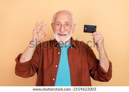 Photo of good mood pensioner man show okay symbol promote recommend credit card isolated on beige color background