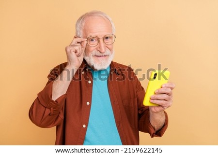 Photo of cheerful good mood pensioner man reading book in his smartphone isolated on beige color background