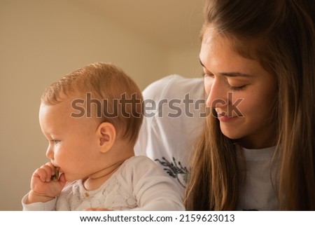 Beautiful mother is watching her baby girl eat the bread