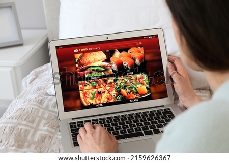 Woman using laptop for ordering food online at home, closeup. Concept of delivery service