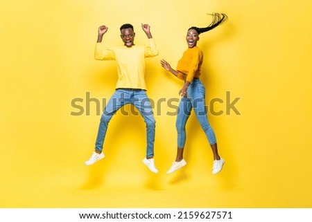 Surprised excited African couple jumping in studio isolated yellow color background Royalty-Free Stock Photo #2159627571