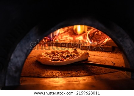 Pizza concept. Preparing traditional italian pizza. Long shovel for pizza, baking dough in a professional oven with open fire in interior of modern restaurant kitchen