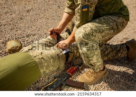 Army medics practice applying a tourniquet to the leg of a wounded soldier. Combat tactical equipment. Combat use Turnstile. The concept of military medicine. Royalty-Free Stock Photo #2159634317