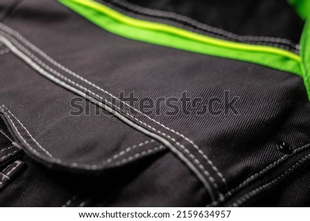 White stitching on black fabric. Texture of black working clothes with white stitching closeup, green reflective elements