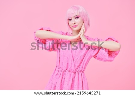 Beauty, fashion. Portrait of a cute teen girl with bright pink makeup and pink hair smiling and posing in fashionable pink dress. Pink background. 