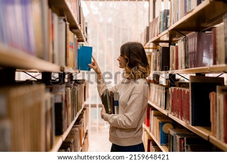 Beautiful girl taking a book while standing in a library