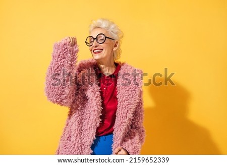 Happy and playful mature woman dancing, smiling and having fun. Photo of elderly woman above 70 years old in stylish outfit on yellow background Royalty-Free Stock Photo #2159652339