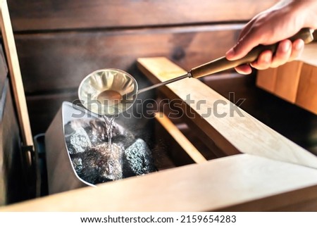 Sauna in Finnish spa. Hot steam, water on stones. Man in wellness and health room in Finland. Warm temperature bath therapy. Traditional summer cabin relaxation. Royalty-Free Stock Photo #2159654283