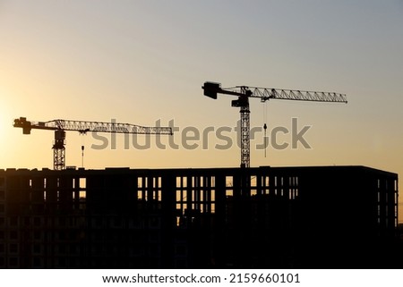 Silhouette of two towers crane above unfinished building at sunrise. Housing construction, apartment block in city on background