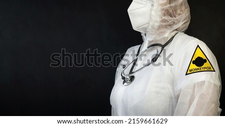 MONKEYPOX. A doctor in a protective suit against smallpox. A sign with a sign of danger and a monkey. Virus, epidemic, disease. Black background. Royalty-Free Stock Photo #2159661629