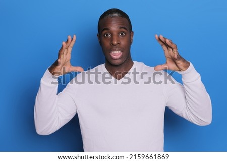 Young African American man pictured isolated on blue background with hands near head