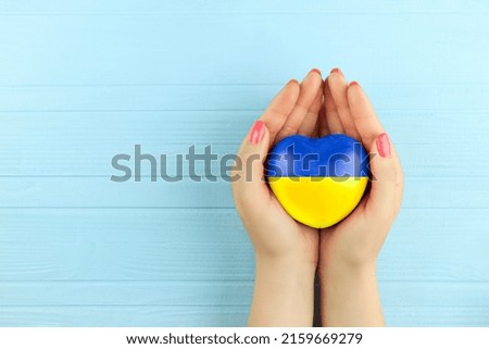 female hands holding a painted heart in the Ukrainian flag
