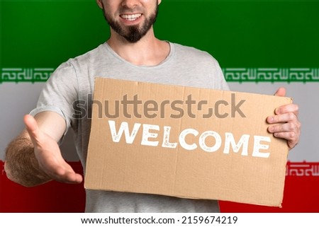 The concept of tolerance for immigrants and people of different life positions. A man holds a cardboard and stretches out his hand to greet. Flag of Iran. Text Welcome.