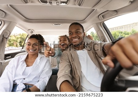 Excited Black Family Driving New Auto, Daughter Pointing Finger Showing Destination Of Road Trip. Parents And Kid Traveling On Vacation By Car Enjoying Ride Outdoors. Selective Focus Royalty-Free Stock Photo #2159675223