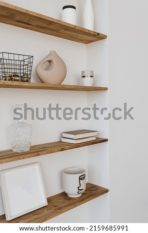 Decorated shelf on white wall. Aesthetic luxury minimalist home interior design decoration. Elegant Scandinavian, hygge style interior. Picture frames, fragrance, vase, books, candle