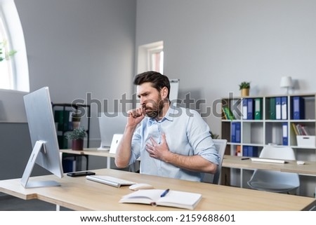 Sick man working in the office, has a bad cough, coughing businessman at the computer Royalty-Free Stock Photo #2159688601