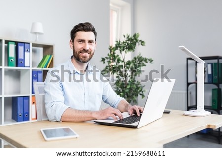 Happy businessman working in bright modern office behind laptop man with beard smiling and looking at cameras Royalty-Free Stock Photo #2159688611