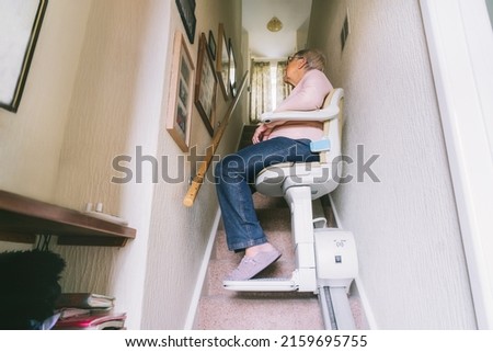 Senior woman using automatic stair lift on a staircase at her home. Medical Stairlift for disabled people and elderly people in the home. Selective focus Royalty-Free Stock Photo #2159695755