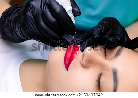 a close-up of the lip tattoo procedure using the master tattoo machine circles the corners of the lips Royalty-Free Stock Photo #2159697049