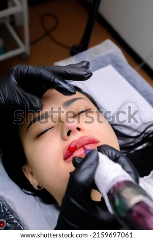 the cosmetology room undergoes a permanent lip makeup procedure, the master applies a tattoo using a tattoo machine Royalty-Free Stock Photo #2159697061