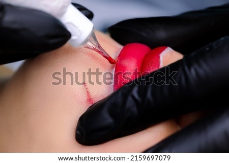 the master in black gloves rolls up the lips of the model and stretches them to apply the contour with the help of a tattoo machine Royalty-Free Stock Photo #2159697079