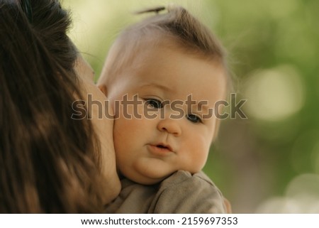 A close portrait of a 7-month girl who is been kissing by her mother in the park