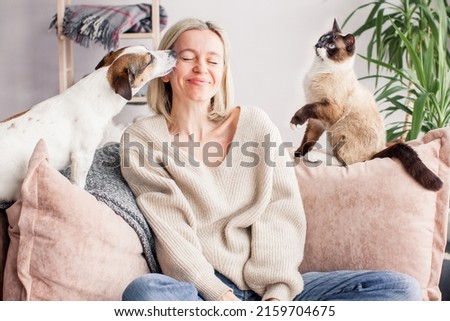 Woman closed her eyes with pleasure spending time with pets Happy woman is resting on the couch with a dog and a cat Royalty-Free Stock Photo #2159704675