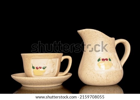 One ceramic cup on a saucer and a milk jug, close-up isolated on a black background.