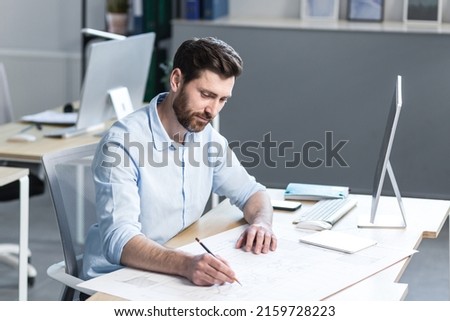 Young male architect, designer making drawings and project on whatman paper on desk in his office. Sitting at a table, with a computer, focused