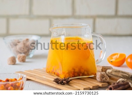 Hot drink, sea buckthorn tea with tangerine slices in a transparent glass teapot on a light concrete background. Hot drink recipes. Sea buckthorn recipes