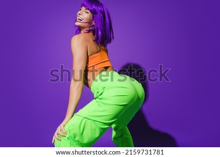 Carefree woman dancer wearing colorful sportswear twerking against purple background