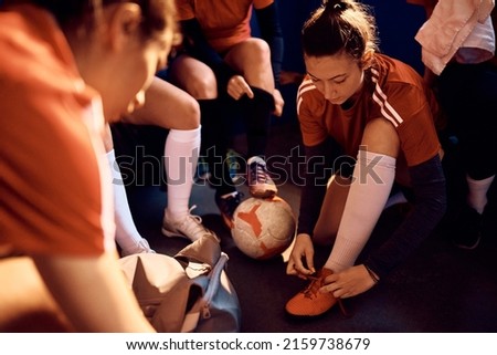 Female soccer team dressing up for sports match in locker room. Focus is on woman tying shoelace.  Royalty-Free Stock Photo #2159738679