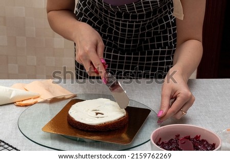 Leveling the cream on the sponge cake with spatula. There is bowl with stuffing on the table. The process of making cake. Selective focus. Picture for articles about food, confectioners.